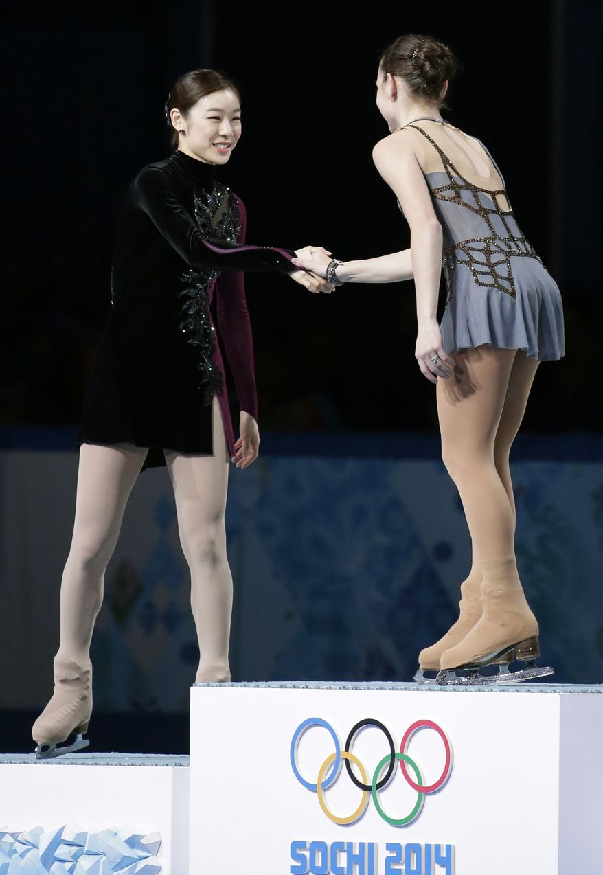 Yuna Kim of South Korea, left, shakes hands with Adelina Sotnikova of Russia as they stand on the podium during the flower ceremony for the women's free skate figure skating finals at the Iceberg Skating Palace during the 2014 Winter Olympics, Thursday, Feb. 20, 2014, in Sochi, Russia. Sotnikova placed first, followed by Kim and Kostner. (AP Photo/Bernat Armangue)