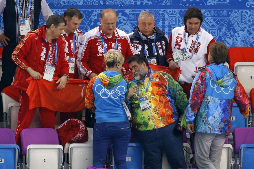 Mikhail Kusnirovich, founder and chairman of Russian apparel giant Bosco Di Ciliegi, bottom row center, speaks with the protocol manager at the Iceberg Skating Palace in Sochi, Russia, after she tried to stop Russian Communist Party leader Gennady Zyuganov, top center, and Communist lawmakers Yuri Afonin, second left, and Nikolai Kharitonov, second right, from displaying the Soviet Banner of Victory during a flower ceremony for the short track speedskating competition at the 2014 Winter Olympics on Friday, Feb. 21, 2014. The banner is a replica of the flag raised by Soviet soldiers in Berlin in 1945, in victory over Nazi Germany. The International Olympic Committee forbids the display of political banners at Olympic venues. Communist party spokesman Alexander Yushchenko is at top right. (AP Photo/Vadim Ghirda)