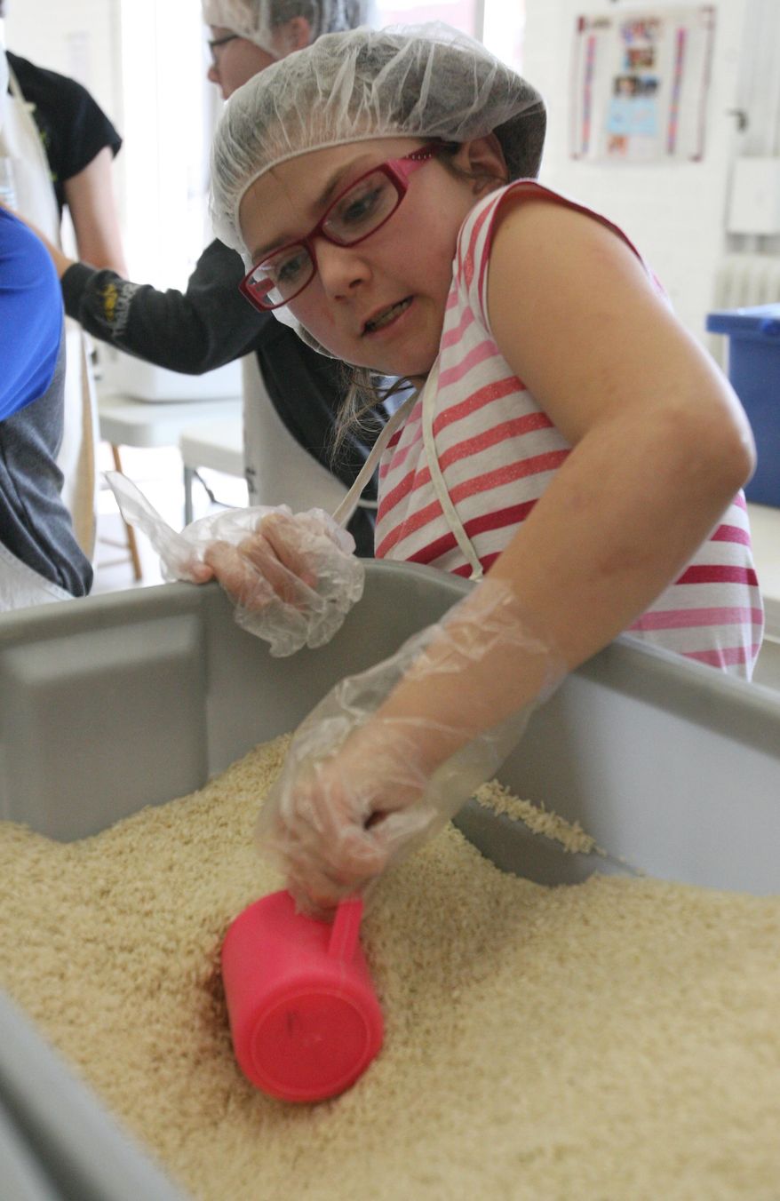 Watson Elementary School fifth-grader Lindsey Clevenger scoops up rice to put into a meal packet while volunteering for Kids Against Hunger Tuesday, Feb. 18, 2014. (AP Photo/The Hastings Tribune, Amy Roh)
