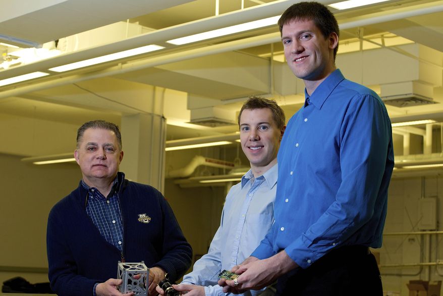 In this undated photo provided by Marquette University, Robert Bishop, Opus Dean of Marquette University College of Engineering, left, senior Devin Turner, center, and mechanical engineering graduate student Peter Jorgensen, pose for photos holding components of Marquette’s first CubeSat satellite, at the Marquette Spacecraft Engineering Lab on the university’s campus in Milwaukee. Marquette University is one of 16 institutions that received permission from NASA this month to launch small, coffee mug-sized satellites into space to collect data.(AP Photo/Marquette University, Jesse Lee)