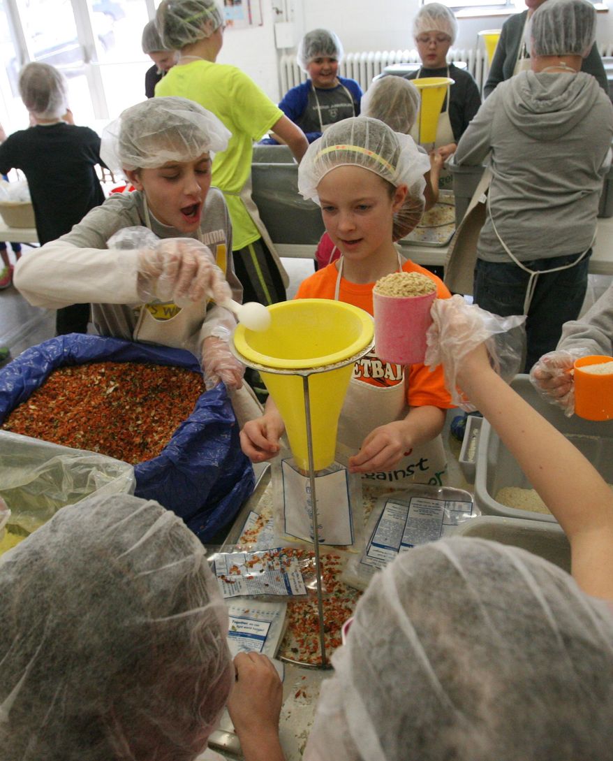 Watson Elementary School fifth-grader Matthew Hansen, left, pours seasonings into a packet held by classmate Brittany Ochsner Tuesday, Feb. 18, 2014. while volunteering for Kids Against Hunger. (AP Photo/The Hastings Tribune, Amy Roh)
