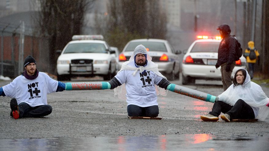 Protesters Joe Hiller, left, Milton Cornejo, center and Maru Mola, right sit chained together blocking the road in front of the federal Northwest Detention Center in the Tacoma Tideflats, Monday, Feb 24, 2014. Organizers with the Not One More Deportation campaign say they want to draw attention to deportations that break up families. They complain the Obama administration has deported more people than the previous Bush administration. (AP Photo/The News Tribune, Joe Barrentine)