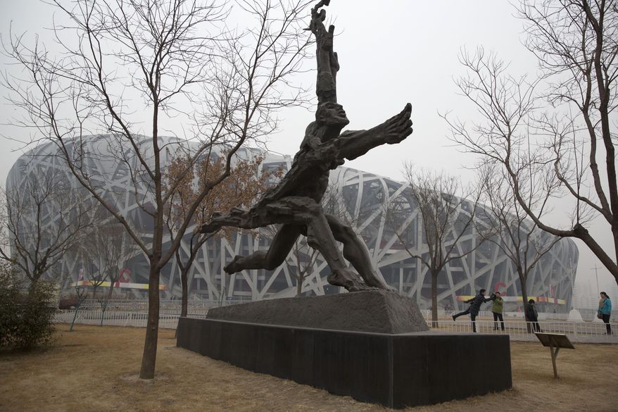 In this picture taken, Sunday, Feb. 23, 2014, a tourist poses near giant sculptures near the iconic Bird's Nest National Stadium in Beijing, China. The National Stadium, nicknamed the Bird’s Nest because of its lattice design, has become a key Beijing landmark and a favored backdrop for visitors' snapshots. But few tourists are willing to pay more than $8 to tour the facility as enthusiasm for the 2008 Games fades, and the venue has struggled to fill its space with events. Beijing, which spent more than $2 billion to build 31 venues for the 2008 Summer Games, is reaping some income and tourism benefits from two flagship venues, though many sites need government subsidies to meet hefty operation and maintenance costs. (AP Photo/Ng Han Guan)