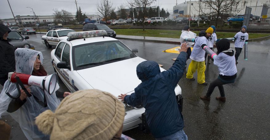 A Tacoma Police Officer uses his vehicle to move Enrique Agular out of the way as protesters block the road in front of the federal Northwest Detention Center Monday, Feb. 24, 2014 in Tacoma, Wash. Organizers with the Not One More Deportation campaign say they want to draw attention to deportations that break up families. They complain the Obama administration has deported more people than the previous Bush administration. (AP Photo/The News Tribune, Joe Barrentine)