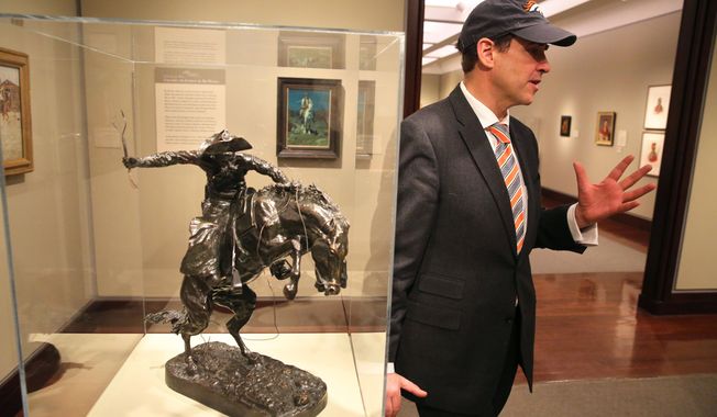 FILE - In this Jan. 27, 2014 file photo, Denver Art Museum Director Christoph Heinrich leans against a Frederic Remington bronze statue of a cowboy riding a bucking horse, part of a collection on display at the Denver Art Museum. The museum is packing up the prized statue to send it to the Seattle Art Museum after losing a friendly Super Bowl bet.  The Seattle Seahawks beat the Denver Broncos 43-8, and the Remington will go to Seattle for three months. (AP Photo/Brennan Linsley, File)