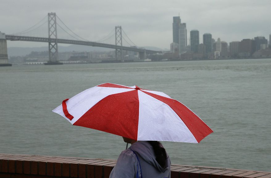 A women walks along Treasure Island with the San Francisco Bay bridge in the background during a rain storm Wednesday, Feb. 26, 2014, in San Francisco. Several winter storms are expected to bring rain to the Bay Area through the end of the week. (AP Photo/Ben Margot)