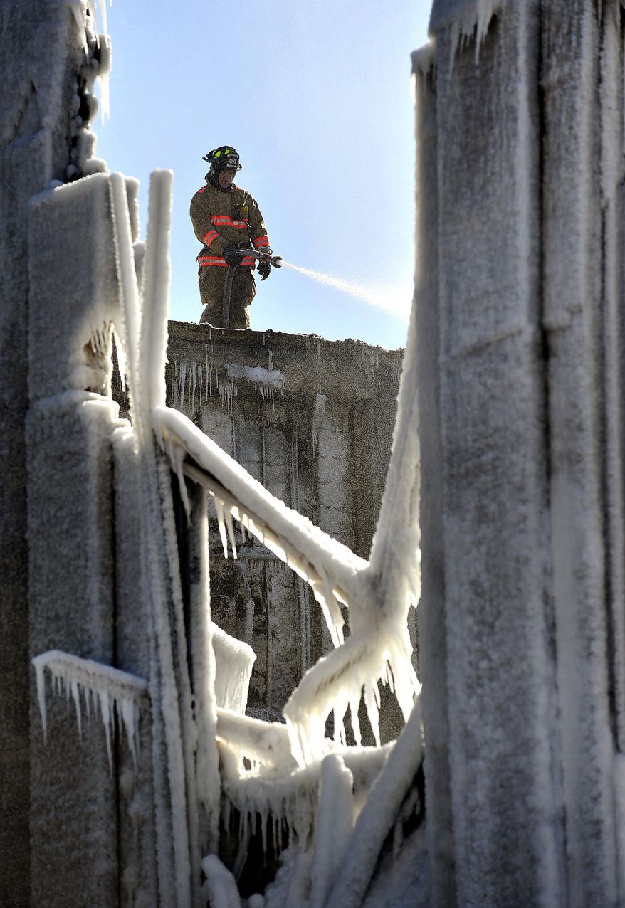 A firefighter trains a hose on hot spots while surrounded by ice after an early morning fire at Mitchell Elementary School in Racine, Wis., Thursday, Feb. 27, 2014. The fire severely damaged the school, causing the gymnasium roof to collapse. School administrators have canceled classes at the damaged school. (AP Photo/The Journal Times, Scott Anderson)