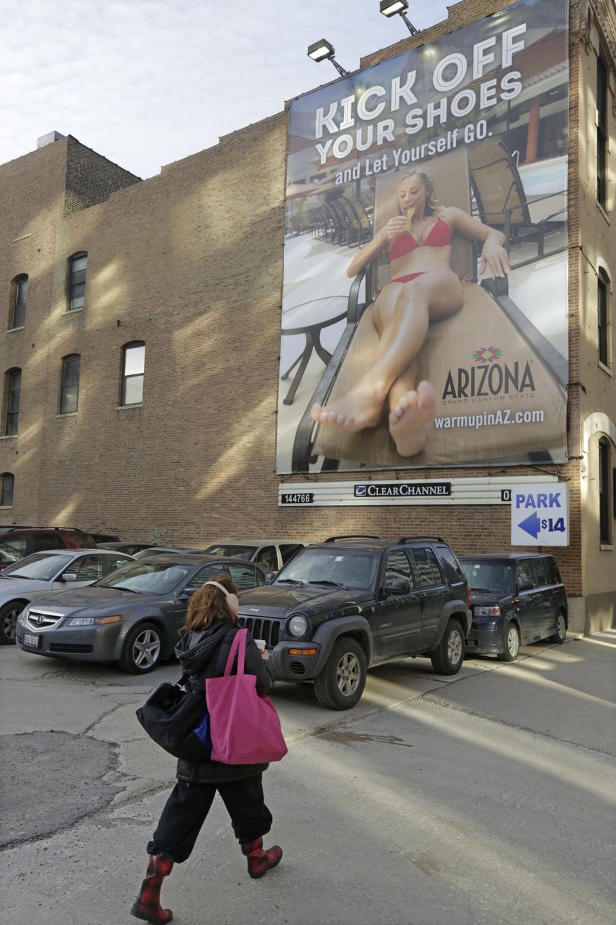 In this Wednesday, Feb. 26, 2014 photo, a pedestrian in Chicago walks bundled up for the cold weather past an advertisement touting the warmth of Arizona. With yet another polar vortex like storm system bearing down on many parts of the country, suffering Midwesterners dream about being anywhere but home. Tourist operations have been fueling this with email and other ad campaigns dangling a little sunshine and beach scenes in front of us. (AP Photo/M. Spencer Green)