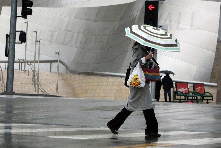 A pedestrian covers from the rain as she makes her way past the Disney Music Center in downtown Los Angeles on Friday, Feb. 28, 2014. The first wave of a powerful Pacific storm spread rain and snow early Friday through much of California, where communities endangered by a wildfire just weeks ago now faced the threat of mud and debris flows.(AP Photo/Richard Vogel)