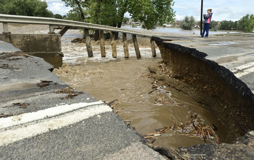 In this photo taken on Sept. 13, 2013, a woman takes photos of a guard rail at a flood damage bridge on County Line Road outside Longmont Colo., during the height of major flooding in the state. Nesting bald eagles have prompted the delay of the bridge rebuilding project near Longmont, while local officials try to comply with federal regulations protecting endangered species. (AP Photo/The Daily Times Call, Matthew Jonas) NO SALES, MAGS OUT, TV OUT, MANDATORY PHOTO CREDIT: NEWSPAPER AND PHOTOGRAPHER