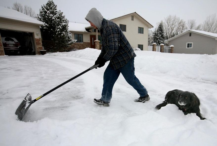 Tom Grismer shovels snow from his driveway on Loma Vista Drive, as his dog Rocky sits by him, as a snowstorm hits the area Friday, Feb. 28, 2014, in Billings, Mont. (AP Photo/The Billings Gazette, Casey Page)