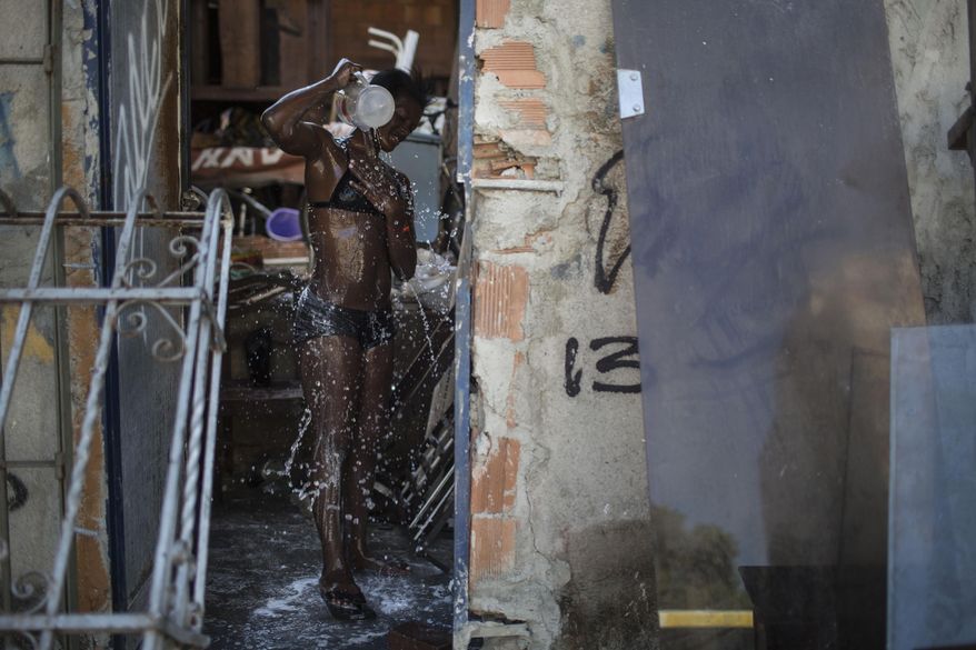 In this Jan. 10, 2014 photo, a woman takes a shower using a bucket of water inside the Favela do Metro slum outside Maracana stadium where homes have been demolished and residents evicted in Rio de Janeiro, Brazil. Some residents were evicted from their homes two years ago for the area to be renovated for this year's World Cup and 2016 Olympics, but people reoccupied the homes and are fighting to stay. (AP Photo/Felipe Dana)