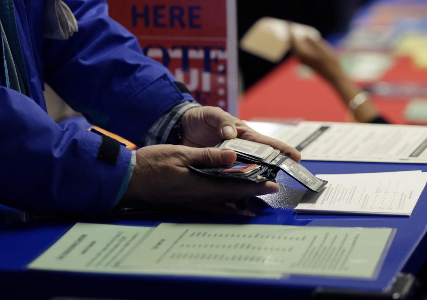 In this Wednesday, Feb. 26, 2014 photo, a voter shows his photo identification to an election official at an early voting polling site, in Austin, Texas. In elections that begin next week, voters in 10 states will be required to present photo identification before casting ballots _ the first major test of voter ID laws after years of legal challenges arguing that the measures are designed to suppress voting. (AP Photo/Eric Gay)