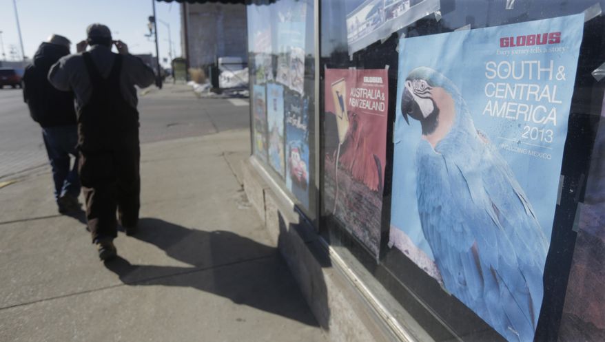 In this Wednesday, Feb. 26, 2014 photo, bundled up pedestrians walk past an advertisement for South America and Central America in the window of a travel agency in Blue Island, Ill. With yet another polar vortex like storm system bearing down on many parts of the country, suffering Midwesterners dream about being anywhere but home. Florida resorts and other tourist operations have been fueling this with email and other ad campaigns dangling a little sunshine and beach scenes in front of us. (AP Photo/M. Spencer Green)