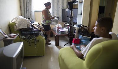 In this Feb. 16, 2014 photo, Dalvaneide Pequeno do Nascimento organizes her apartment as her son looks on at their residence inside the Condominio Oiti project in the suburb of Campo Grande, Rio de Janeiro, Brazil. Nascimento, her husband and children were among the families forced out of their homes in Vila Recreio II, a Rio de Janeiro slum that was razed three years ago to make way for the Transoeste expressway connecting the Barra da Tijuca neighborhood that’ll be the main hub for the 2016 Olympics with the western outskirts of Rio. (AP Photo/Leo Correa)