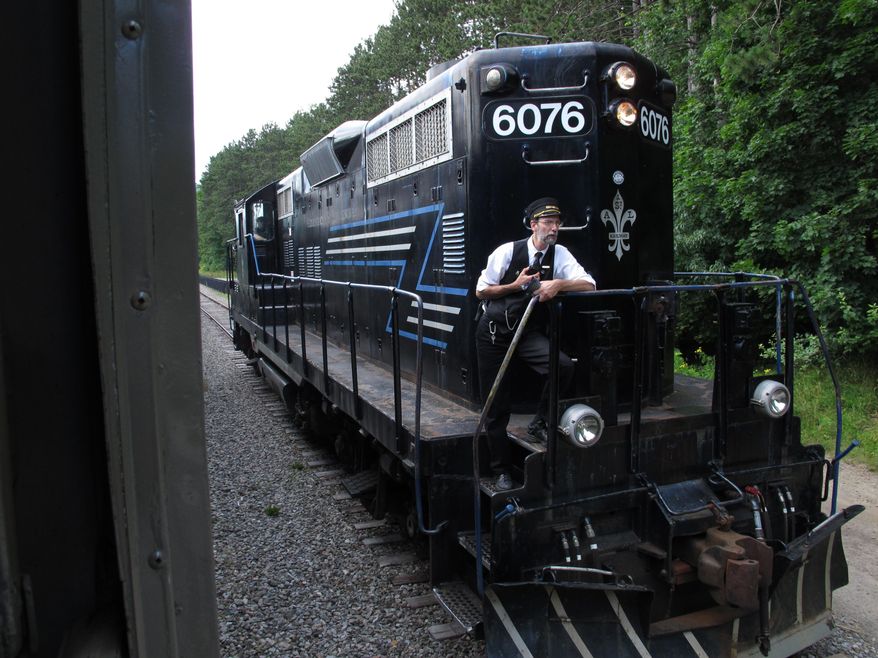 FILE - FILE - In this July 26, 2013 file photo, Paul Erena, a volunteer conductor for the Adirondack Scenic Railroad, rides on an engine as it is switched to the front of the train at the Lake Placid, N.Y. station. Backers of a proposed 90-mile biking, hiking and snowmobiling trail following a rail bed through the heart of the Adirondacks are frustrated at the Cuomo administration’s slow pace deciding whether to open a review needed to move forward. At issue is whether to spend millions of dollars on track repairs to extend a scenic railroad or replace the tracks with a multi-use trail on the state-owned corridor from Old Forge to Lake Placid. (AP Photo/Mary Esch, File)