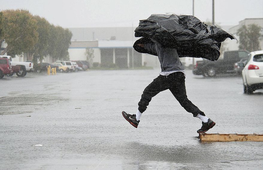 Manufacturing Assembly worker Terry Young, 24, of Rialto, Calif., uses a sheet of plastic to protect himself from a downpour Friday, Feb. 28, 2014, as he jumps a flooded parking lot from a wood pallet to get to a food truck during his break in Anaheim, Calif. The first wave of a powerful Pacific storm spread rain and snow early Friday through much of California, where communities endangered by a wildfire just weeks ago now faced the threat of mud and debris flows. (AP Photo/The Orange County Register, Ken Steinhardt) MAGS OUT; LOS ANGELES TIMES OUT