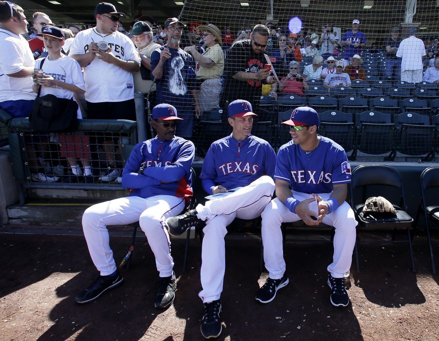 Texas Rangers' Ron Washington and bench coach Tim Bogar, center, talk with Seattle Seahawks quarterback Russell Wilson, right, before the start of a spring training exhibition baseball game against the Cleveland Indians, Monday, March 3, 2014, in Surprise , Ariz. (AP Photo/Tony Gutierrez)