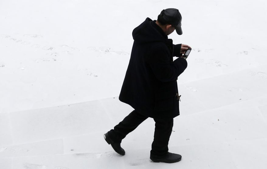 A man checks his mobile phone as he walks through snow-covered Columbus Park, Monday, March 3, 2014 in New York. Winter kept its icy hold on much of the country Monday, with snow falling and temperatures starting to plummet from the Mid-Atlantic states up to the East Coast. (AP Photo/Mark Lennihan)