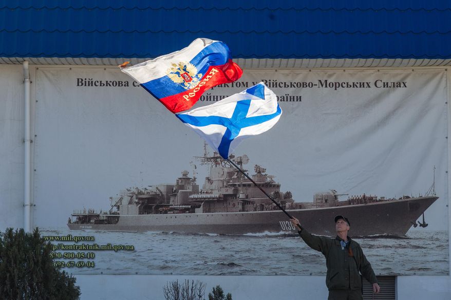 A pro-Russian activist waves the Russian state, upper, and Russian Navy flags outside an entrance to the General Staff Headquarters of the Ukrainian Navy in Sevastopol, Ukraine, Monday, March 3, 2014. Pro-Russian soldiers seem to further cement their control over the strategic region — that also houses the Russian Black Sea Fleet — by seizing a ferry terminal in the Ukrainian city of Kerch about 20 kilometers (12 miles) by boat to Russia, intensifying fears that Moscow will send even more troops into the peninsula. It comes as the U.S. and European governments are trying to figure out ways to halt and reverse the Russian incursion. (AP Photo/Andrew Lubimov)