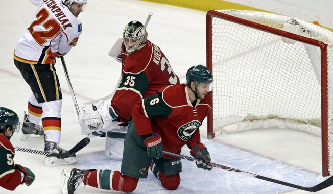 Minnesota Wild goalie Darcy Kuemper, center, looks to teammate Marco Scandella, right, to clear away the puck as Calgary Flames&#x27; Lee Stempniak, left, stands near in the first period of an NHL hockey game, Monday, March 3, 2014, in St. Paul, Minn. (AP Photo/Jim Mone)