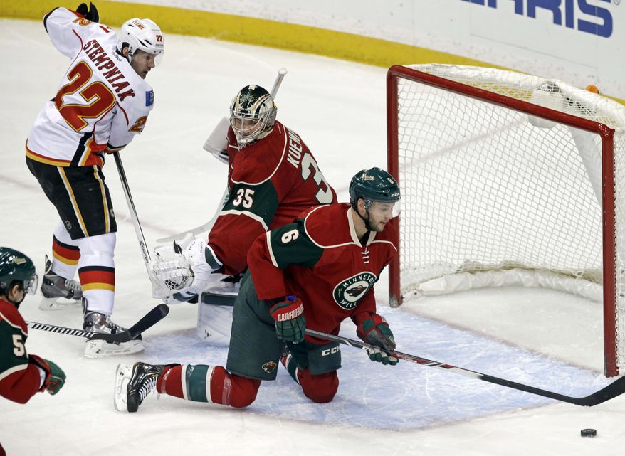 Minnesota Wild goalie Darcy Kuemper, center, looks to teammate Marco Scandella, right, to clear away the puck as Calgary Flames' Lee Stempniak, left, stands near in the first period of an NHL hockey game, Monday, March 3, 2014, in St. Paul, Minn. (AP Photo/Jim Mone)