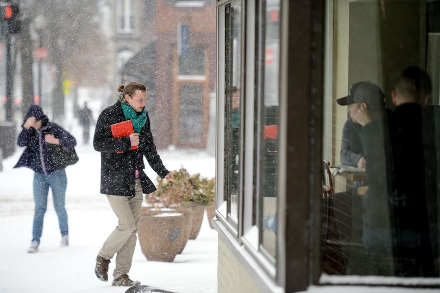 Steve Guilday of Washington, D.C., right, sits in the window of Bistro Bohem in Shaw and watches pedestrians in the snow as the region gets 6-8 inches of snow, Washington, D.C., Monday, March 3, 2014. (Andrew Harnik/The Washington Times)