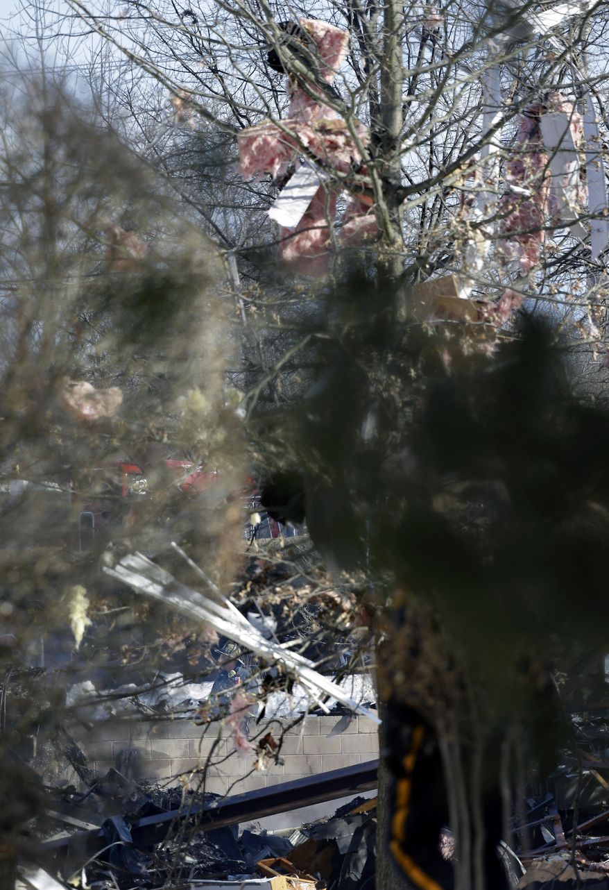 Debris is seen in the trees, as a firefighter, center back, looks through rubble after an explosion at a townhouse complex Tuesday, March. 4, 2014, in Ewing, N.J. Authorities say just three of seven people hurt in the gas explosion will need to be admitted to a hospital, and a hospital official says none has life-threatening injuries. PSE&G crews were repairing a gas line damaged by a private contractor when the gas ignited at the suburban town house development. (AP Photo/Mel Evans)