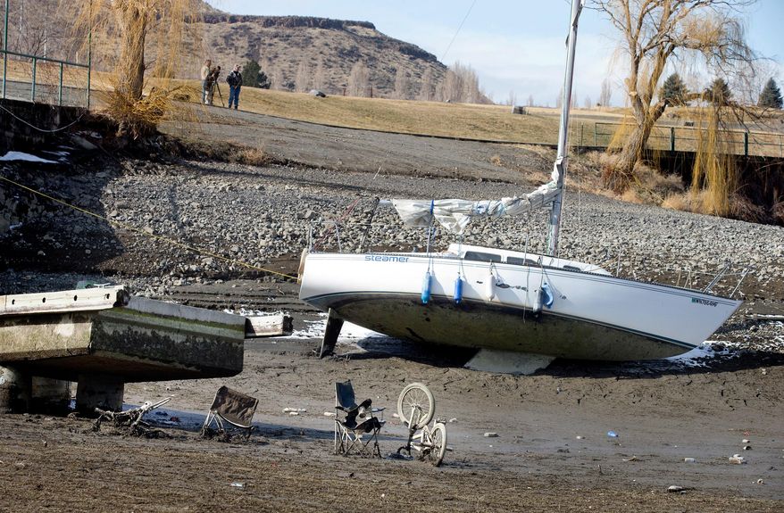 A sailboat owned by Bryan Stockdale, of Vantage, Wash., is left in the mud at the Vantage Riverstone Resort dock in Vantage on Monday, March 3, 2014, as up to 20 feet of water is let out of the Columbia River reservoir behind Wanapum Dam after a spillway pillar was discovered to be cracked at the dam last week. Garbage is seen that had been left in the water at the end of the dock. (AP Photo/The Wenatchee World, Don Seabrook)