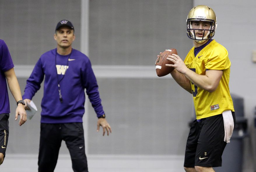New Washington head football coach Chris Petersen, left, stands near redshirt quarterback Jeff Lindquist, right, as Lindquist passes on the first day of spring NCAA college football practice, Tuesday, March 4, 2014, in Seattle. (AP Photo/Ted S. Warren)