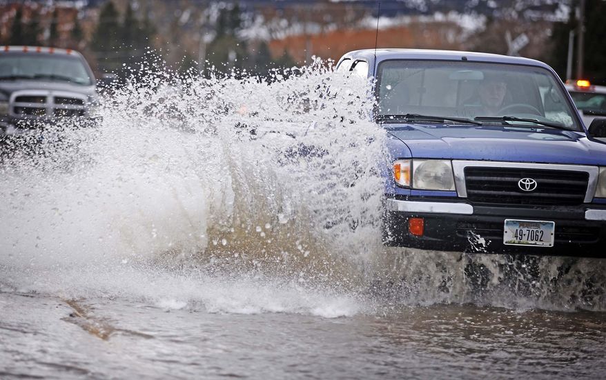 Water sprays up from cars along Park Street in front of the Town & Country Foods grocery story as water floods the street Thursday, March 6, 2014 in Livingston, Mont. The city of Livingston declared a state of emergency after melting snow flooded creeks and ditches and sent water running down city streets. (AP Photo/Livingston Enterprise, Shawn Raecke)