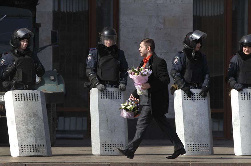 A man carries bouquets of flowers as riot police stand at the entrance of the regional administrative building in Donetsk, Ukraine, Friday, March 7, 2014. Clashes between protesters and police broke out early Thursday in Donetsk as police cleared demonstrators from the regional administration center. The Ukrainian flag once again was hoisted over the building, and about 100 Ukrainian Interior troops could be seen in and around it. (AP Photo/Sergei Grits)