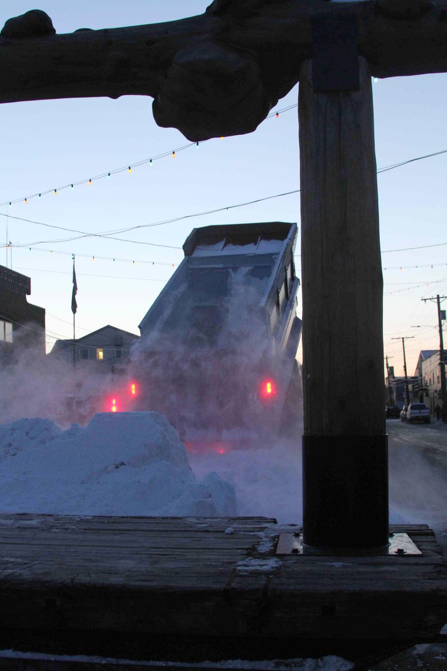 A Nome public works truck dumps a load of snow onto Front Street on Sunday, March 9, 2014, in Nome, Alaska. The snow was trucked in to provide a trail for mushers to the finish line of the Iditarod Trail Sled Dog Race. The wooden frame is the famed burled arch finish line. (AP Photo/Mark Thiessen)