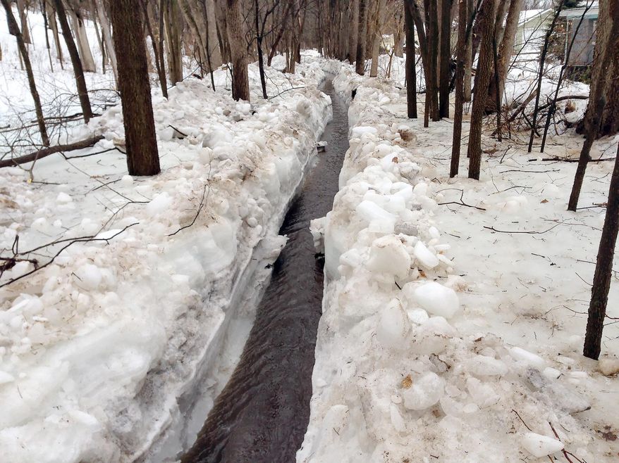 In this photo taken on Tuesday March 11, 2014, water flows through Sand Lake Coulee Creek in the town of Onalaska, Wis., after crews used dynamite to help clear up to five feet of ice. After the blast, crews dug out the ice and created a channel for the water. (AP Photo/The La Crosse Tribune, Chris Hubbach)