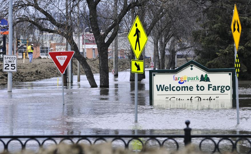FILE - In this April 8, 2011 file photo, a welcome sign for Fargo, N.D., sits in the rising floodwaters of the Red River as a flood engineer for the U.S. Army Corps of Engineers, at left, inspects the levee protecting the downtown area. The Red River Diversion Authority is meeting Thursday, March 13, 2014, in Fargo for the first time since President Obama left the project out of his budget plans. The $2 billion channel would move water around Fargo and neighboring Moorhead, Minn., which has prepared for major floods in four of the last five years. (AP Photo/Jim Mone, File)