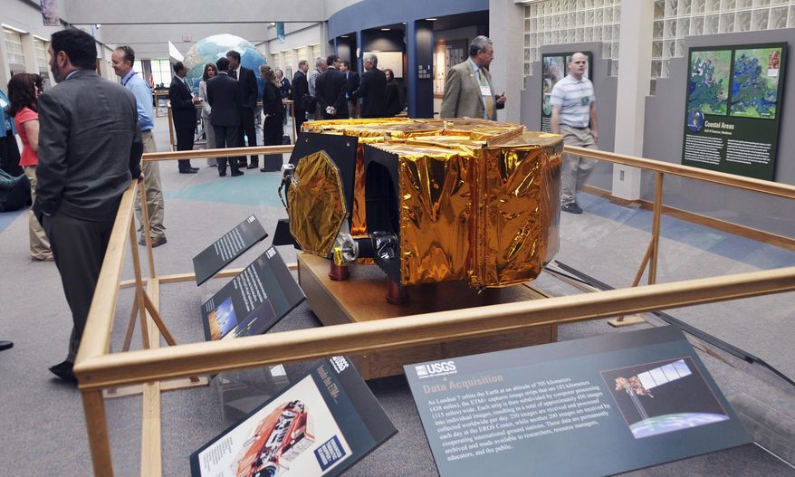 FILE - In this May 30, 2013 file photo, visitors and staff at the U.S. Geological Survey's Earth Resources Observation and Science Center, EROS, gather near a scale model of the Landsat 7 satellite. The facility is helping in the international search for a missing Malaysian jetliner. EROS collects, archives and makes available for download more than 400 data-filled images of the Earth each day. The images coming from EROS have not produced any solid leads in the case of the missing plane, but the center's Disaster Response Coordinator Brenda Jones said she hopes the center's work eventually will help lead to answers. (AP Photo/Dirk Lammers, File)