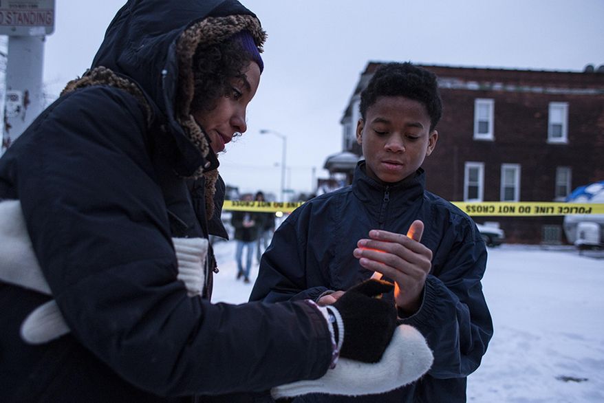 Katie Hearn, Heidelberg Project marketing coordinator, left, lights a candle for Kobe Jones, 12, during a vigil at the site of the latest fire at the Heidelberg Project in Detroit, Thursday, March 13, 2014. A March 7 fire destroyed a house covered in stuffed animals and dolls that was part of the Heidelberg Project. It was the latest casualty in a 10-month string of suspicious fires at houses that are part of the interactive outdoor art installation. Tyree Guyton founded the Heidelberg Project on Detroit's east side in 1986 as a response to urban decay. (AP Photo/The Saginaw News, Katie Bailey) ALL LOCAL TV OUT; LOCAL TV INTERNET OUT