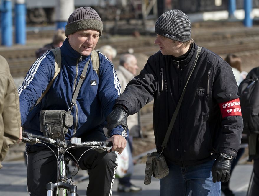 A member of the Crimean self defense stops a man at the main railway station in Simferopol, Ukraine, Friday, March 14, 2014. Members of the Crimean self defense forces check the luggage and identity documents of passengers arriving by train, especially from western Ukrainian cities or the capital, to Simferopol, looking for what they label as provocateurs, ahead of the March 16 referendum that will ask residents if they want the territory to become part of Russia. (AP Photo/Vadim Ghirda)