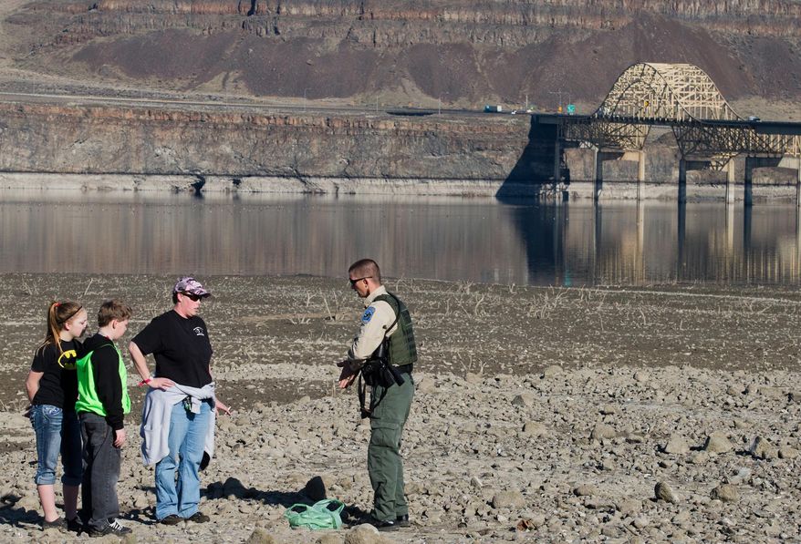 Washington State Department of Fish & Wildlife officer Will Smith warns Talena Hunter of Ellensburg, Wash., and her two children to stay off the exposed beach area along the Columbia River on Wednesday, March 12, 2014. The group was looking for exposed debris near Vantage. Grant County PUD is paying for patrols along the Columbia to warn people to stay above the high water mark for their own safety and to protect cultural sites. (AP Photo/Wenatchee World/Mike Bonnicksen)
