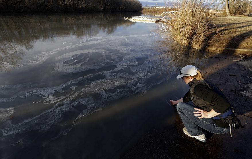 FILE - In this Wednesday, Feb. 5, 2014 file photo, Amy Adams, North Carolina campaign coordinator with Appalachian Voices dips her hand into the Dan River in Danville, Va. as signs of coal ash appear in the river. Documents and interviews collected by The Associated Press show how Duke’s lobbyists prodded Republican legislators to tuck a 330-word provision in a regulatory reform bill running nearly 60 single-spaced pages. Though the bill never once mentions coal ash, the change allowed Duke to avoid any costly cleanup of contaminated groundwater leaching from its unlined dumps toward rivers, lakes and the drinking wells of nearby homeowners. (AP Photo/Gerry Broome, File)