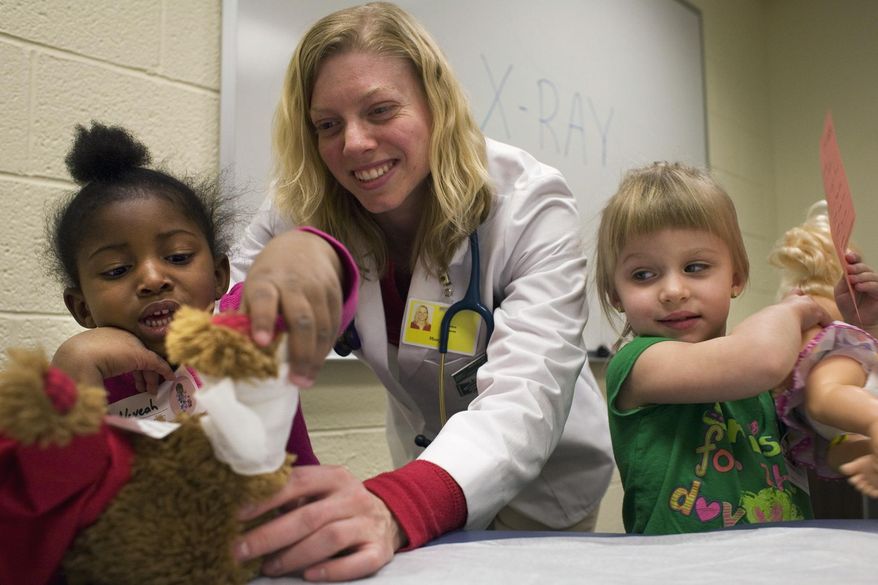 ADVANCE FOR USE SATURDAY, MARCH 22 AND THEREAFTER - In this March 6, 2014 photo, Morgan Echols, a physician assistant graduate student at the Southern Illinois University School of Medicine checks over the dolls belonging to Neveah Shannon, left, and Isabella Pind as part of a doll clinic hosted at the Patient Development Lab of Lindegren Hall on SIU's campus. in Carbondale, Ill. The doll clinic gives children the opportunity to observe scary or threatening medical procedures, without being the subject of those procedures. (AP Photo/The Southern, Steve Matzker)
