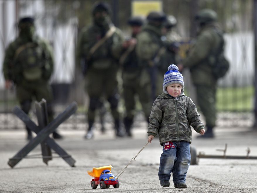 A child drags a toy truck past pro-Russian soldiers standing outside an Ukrainian military base in Perevalne, Crimea, Thursday, March 20, 2014. With thousands of Ukrainian soldiers and sailors trapped on military bases, surrounded by heavily armed Russian forces and pro-Russia militia, the Kiev government said it was drawing up plans to evacuate its outnumbered troops from Crimea back to the mainland and would seek U.N. support to turn the peninsula into a demilitarized zone.(AP Photo/Vadim Ghirda)