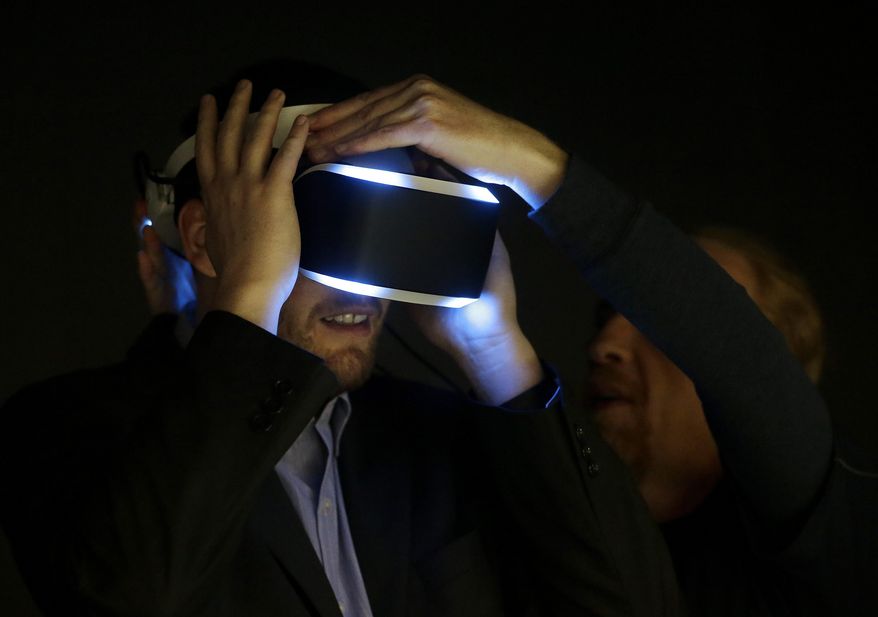 Kevin Joyce, left, gets help putting on the PlayStation 4 virtual reality headset Project Morpheus in a demo area at the Game Developers Conference 2014 in San Francisco, Wednesday, March 19, 2014. (AP Photo/Jeff Chiu)
