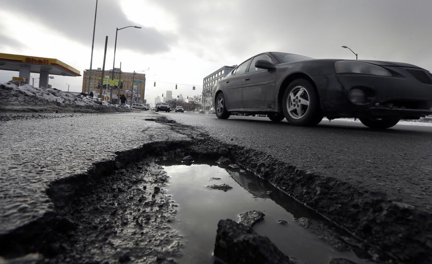 FILE - In this Feb. 11, 2014 file photo a car drives by a pothole in Detroit. As spring officially begins Thursday, officials across much of the nation are still paying the bills for keeping roads clear during the cold, snowy winter. The state expects to spend as much as $140 million for winter maintenance after budgeting just $88 million. (AP Photo/Carlos Osorio, File)