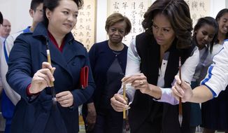 Peng Liyuan, wife of Chinese President Xi Jinping, left, shows U.S. first lady Michelle Obama, center, how to hold a writing brush as they visit a Chinese traditional calligraphy class at the Beijing Normal School, a school that prepares students to go abroad in Beijing, China Friday, March 21, 2014. (AP Photo/Andy Wong, Pool)