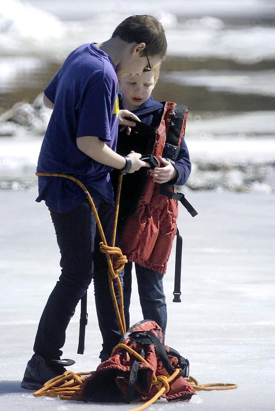 In this Thursday, March 20, 2014 photo, Corbin Crawford, 12, helps his brother Dylan Crawford, 7, put on a life preserver tossed to them by members of the Fort Dodge Fire Department after the pair became stranded on the ice above the Hydroelectric Dam on the Des Moines River near Fort Dodge, Iowa. The boys got stuck on a sheet of ice about 75 feet from the west bank of the river. (AP Photo/The Messenger, Hans Madsen)