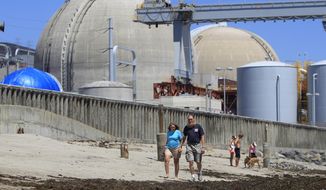 FILE - This file photo taken June 30, 2011, shows beach-goers walking on the sand near the San Onofre nuclear power plant in San Clemente, Calif. Settlement talks are underway to decide who pays the huge bill tied to the shuttered San Onofre nuclear power plant. Edison International — the parent of operator Southern California Edison — disclosed in a government filing Friday, March 21, 2014, that a meeting would be held next week to discuss a possible deal. (AP Photo, Lenny Ignelzi, File)