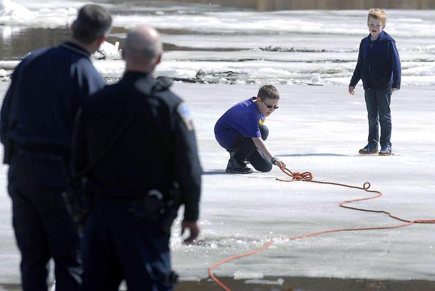 In this Thursday, March 20, 2014 photo, Corbin Crawford, 12, reaches out for a rope tossed to him from shore by a member of the Fort Dodge Fire Department he and his brother, Dylan Crawford, 7, right, became stranded on the ice above the Hydroelectric Dam on the Des Moines River near Fort Dodge, Iowa. The boys got stuck on a sheet of ice about 75 feet from the west bank of the river. (AP Photo/The Messenger, Hans Madsen)