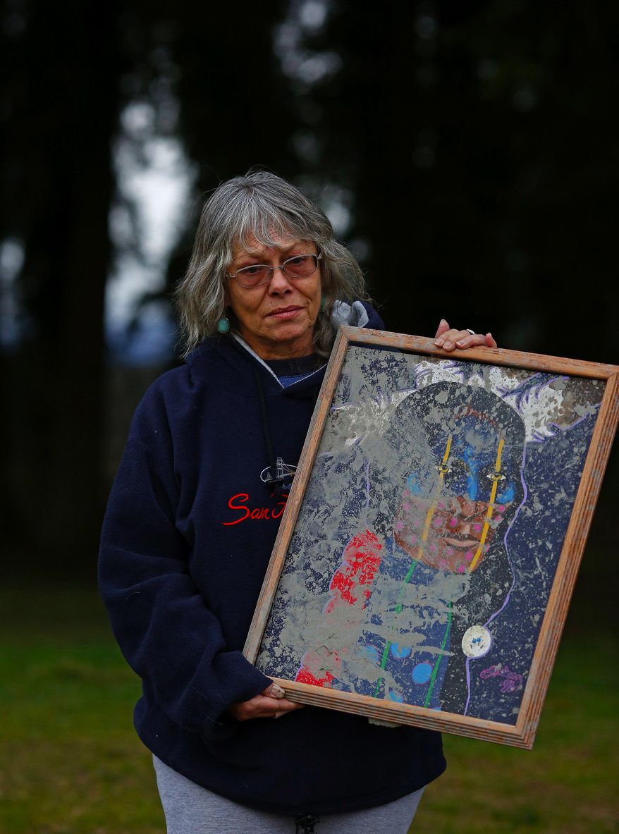 Robin Youngblood survived the landslide that destroyed her house next to the North Fork of the Stillaguamish river Saturday, March 22, 2014. She is holding the only item that survived the disaster, a painting of a Cherokee warrior that was knocked from the wall and muddied. "It saved us." she said. (AP Photo/ The Seattle Times,Mark Harrison) MANDATORY CREDIT TO: Mark Harrison / THE SEATTLE TIMES.