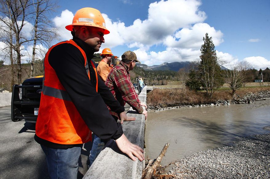 Tom Moff with Snohomish County looks down at the Stillaguamish River as it maintains a low but steady flow off of Whitman Road on Highway 530 on Sunday, March 23, 2014, the day after a giant landslide occurred near mile marker 37 near Oso, Washington. At least six homes have been washed away, with three people reported dead so far and at least eighteen missing. The nearby Stillaguamish River has been dammed up by 15-20 feet of debris as a result, creating more flooding concerns, as reported by KING 5 via the state hydrologist. (AP Photo/The Seattle Times, Lindsey Wasson, Pool)